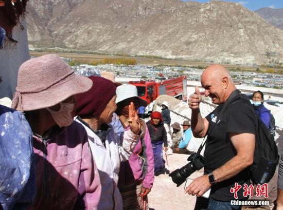 10月23日,来自美国加利福尼亚州的游客Tim游览布达拉宫时,遇到排队上山粉刷的信众,竖起大拇指为他们点赞。中新社记者 赵延 摄